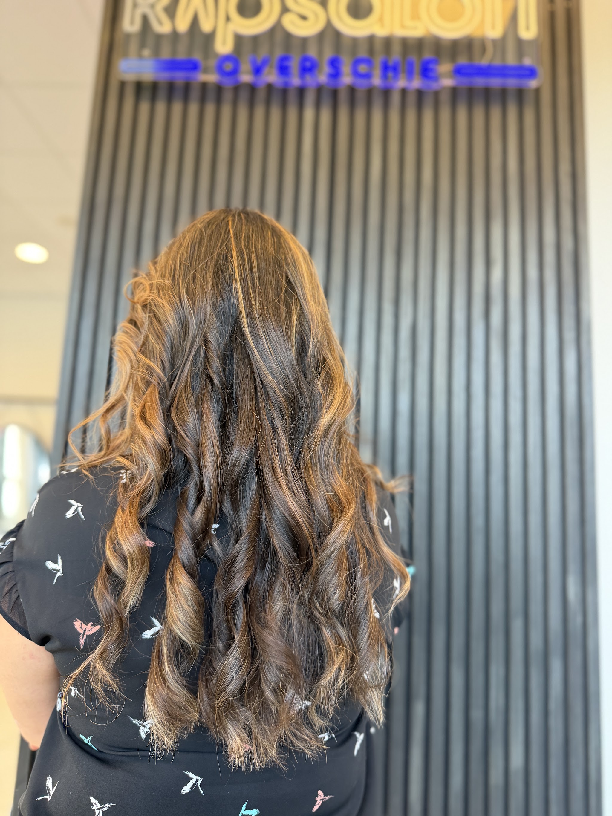 Lang golvend haar met warme highlights, van achteren, voor de neonwand van de salon